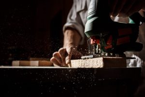 Un artisan menuisier à Seyssel utilise une scie sauteuse pour une coupe précise sur un morceau de bois